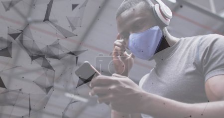 Foto de Red de conexiones contra el hombre afroamericano que usa mascarilla usando smartphone en el gimnasio. - Imagen libre de derechos