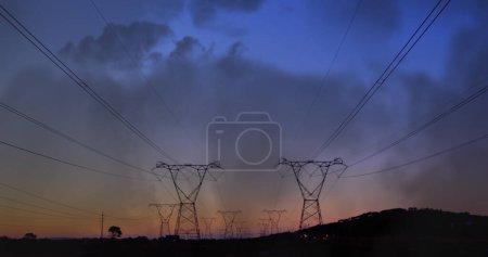 Foto de Compuesto digital de torres de transmisión en un campo durante la puesta del sol, mientras que el fondo muestra nubes - Imagen libre de derechos