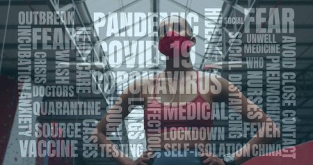 Téléchargez les photos : Texte du concept de coronavirus contre une femme afro-américaine portant un masque facial debout dans la salle de gym. coronavirus covid-19 pandémie et concept de conditionnement physique - en image libre de droit