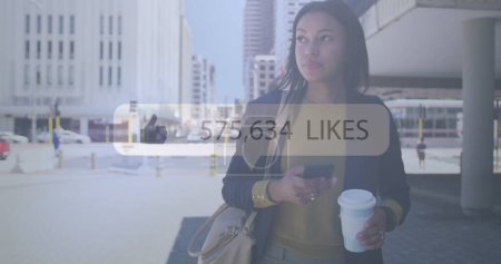 Photo for Image of like thumbs up icon with numbers changing over woman using smartphone in city. digital interface, social media, connection and communication concept digitally generated image. - Royalty Free Image