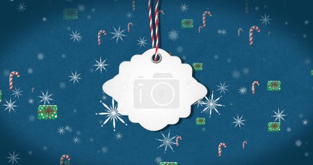 Image of christmas tag with copy space, decorations and snow falling on blue background. Christmas, winter, festivity, tradition and celebration concept digitally generated image.