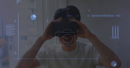 Foto de Interfaz digital con procesamiento de datos contra el hombre asiático que usa auriculares vr en casa. interfaz informática y concepto de tecnología - Imagen libre de derechos
