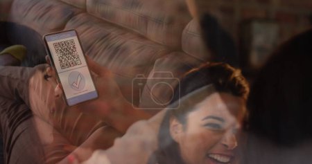 Foto de Mujer sosteniendo un teléfono inteligente con código qr en la pantalla contra amigos animando y viendo partidos deportivos. covid-19 certificado de vacunación y pase de salud con - Imagen libre de derechos