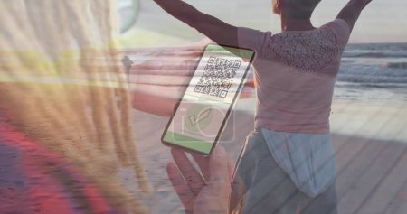 Téléchargez les photos : Image d'une femme tenant un smartphone avec un passeport de vaccination covid 19 sur une femme sur la plage. global covid 19 pandémie et concept de vaccination image générée numériquement. - en image libre de droit
