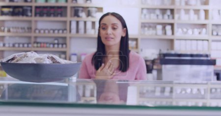 Téléchargez les photos : Une jeune femme biraciale se tient derrière un comptoir dans un magasin. Son regard attentif suggère qu'elle est prête à aider les clients avec leurs besoins. - en image libre de droit
