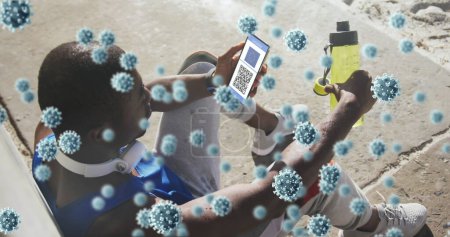 Foto de Composición de las células covid-19 sobre el hombre afroamericano utilizando el teléfono inteligente con código qr en la pantalla. covid-19 certificado de vacunación y concepto de pase sanitario - Imagen libre de derechos