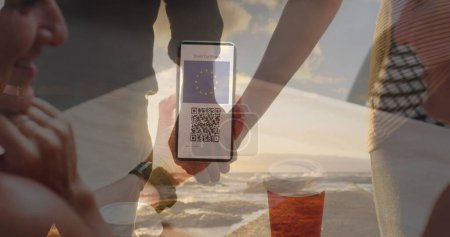 Foto de Mujer sosteniendo un teléfono inteligente con código qr en la pantalla contra una pareja agarrada de la mano en la playa. covid-19 certificado de vacunación y concepto de pase sanitario - Imagen libre de derechos