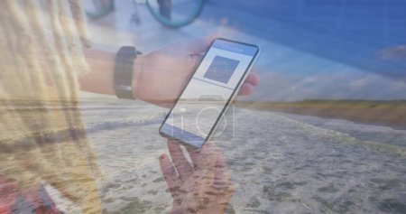 Foto de Composición del hombre sosteniendo un teléfono inteligente con código qr en la pantalla contra la vista aérea de la playa. covid-19 certificado de vacunación y concepto de pase sanitario - Imagen libre de derechos