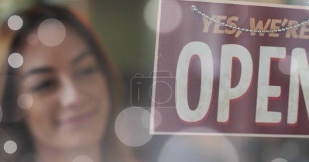 Photo for Image of light spots over caucasian woman opening shop. Global business and digital interface concept digitally generated image. - Royalty Free Image