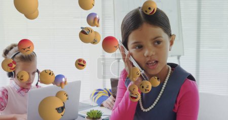 Image of digital interface with emoji icons floating over children using electronic devices. Global computer network technology concept digitally generated image.
