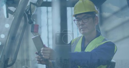 Hombre asiático en equipo de seguridad opera maquinaria en un sitio industrial. Su enfoque en la tarea muestra profesionalidad en un entorno de fabricación.