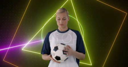 Image of neon scanner processing data and smiling caucasian female football player holding ball. sport, competition and technology concept, digitally generated image.