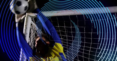Bild einer Spirale der blauen Linie, die sich über einem männlichen Fußballtorwart dreht, der das Tor rettet. Sport- und Wettkampfkonzept, digital generiertes Image.