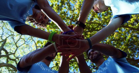 Foto de Diverso grupo de voluntarios apilan las manos al aire libre, con espacio para copias. El trabajo en equipo y el servicio comunitario se enfatizan en este entorno soleado y al aire libre. - Imagen libre de derechos