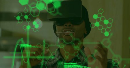 Foto de Imagen de datos científicos en verde flotando en primer plano con un joven mestizo usando un casco VR y tocando la pantalla interactiva con las manos en el fondo - Imagen libre de derechos