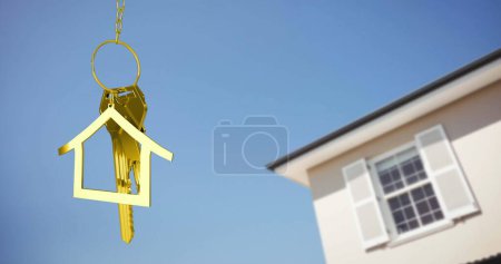 Foto de Imagen de llaves doradas de la casa y llavero en forma de casa colgando sobre una casa y el cielo azul 4k - Imagen libre de derechos