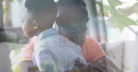 Foto de Imagen de hojas sobre el feliz padre afroamericano y su hijo abrazándose en el sofá. familia, unidad, gasto concepto de tiempo de calidad imagen generada digitalmente. - Imagen libre de derechos