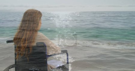 Image de paysage marin sur femme cuacasienne handicapée assise en fauteuil roulant. Journée internationale des personnes handicapées concept image générée numériquement.