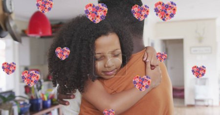 Image of flower hearts over african american father and daughter hugging at home. family life, love and care concept digitally generated image.