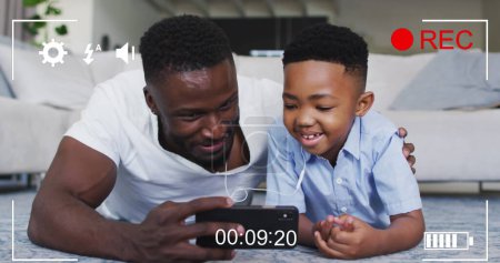 Image of lights over happy african american father and son recording image on smartphone. family, togetherness, spending quality time concept digitally generated image.