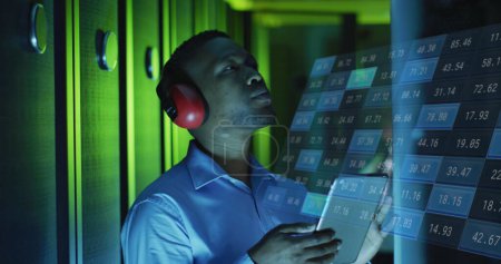 Image of financial data processing over male african american it engineer with tablet. Global business, finances, computing and data processing concept digitally generated image.