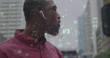 Bild von Netzwerken mit digitalen Ikonen über einem afrikanisch-amerikanischen Mann, der sein Smartphone in der Stadt benutzt. globales soziales Netzwerk, Kommunikations- und Verbindungskonzept digital generiertes Bild.