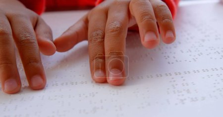 Biracial boy's hands are reading Braille text, with copy space. Close-up view captures the educational moment at school.