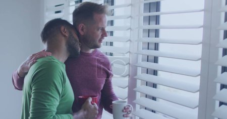 Téléchargez les photos : Couple gay diversifié profite d'un moment calme à la maison, avec espace de copie. Ils partagent une étreinte réconfortante par la fenêtre, reflétant un sentiment d'intimité. - en image libre de droit