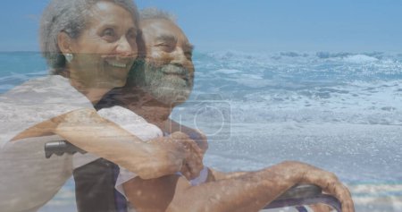 Image of sea landscape over biracial woman and disabled man sitting in wheelchair. International day of persons with disabilities concept digitally generated image.
