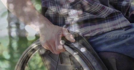 Foto de Imagen de manchas de luz sobre hombre caucásico discapacitado sentado en silla de ruedas. Día internacional de las personas con discapacidad concepto de imagen generada digitalmente. - Imagen libre de derechos