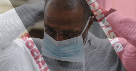 Bild von covid 19 sozialen Distanzierungstext über afrikanisch-amerikanischen Mann, der Gesichtsmaske aufsetzt. Globales Konzept der Coronavirus-Pandemie digital generiertes Bild.