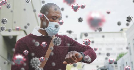 Photo for Covid-19 cells floating against african american senior man wearing face mask checking time. coronavirus covid 19 pandemic. - Royalty Free Image