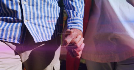 Photo for Image of light moving over midsection of senior couple walking in park holding hands. retirement, domestic life and hope concept digitally generated image. - Royalty Free Image