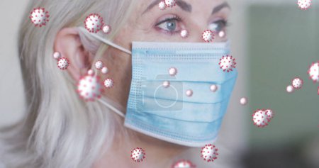 Foto de Imagen de células virales sobre una mujer mayor caucásica con máscara facial. servicios médicos y sanitarios durante coronavirus covid 19 pandemia concepto de imagen generada digitalmente. - Imagen libre de derechos
