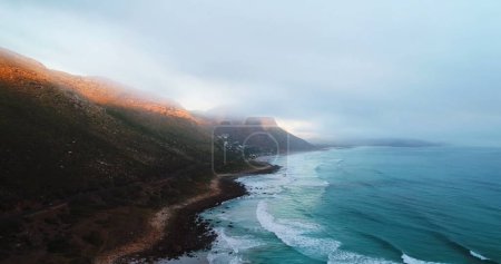 Photo for Coastline meets mountain range under a misty sky. The serene landscape captures the tranquil intersection of land and sea at dawn or dusk. - Royalty Free Image