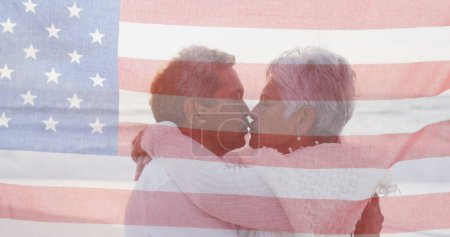 Téléchargez les photos : Image du drapeau des États-Unis d'Amérique sur le couple biracial senior embrassant sur la plage. Patriotisme américain, diversité et concept de tradition image générée numériquement. - en image libre de droit