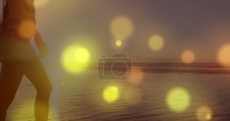 Foto de Manchas amarillas brillantes de luz contra la sección media de una mujer caminando por la playa. Concepto de amor y relación - Imagen libre de derechos