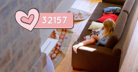 Photo for High angle of a Caucasian woman seated relaxed on a couch while typing on her phone. Above her is a digital image of a heart count bar - Royalty Free Image