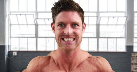 Cara de cerca de un hombre caucásico sin camisa flexionando sus músculos en el gimnasio