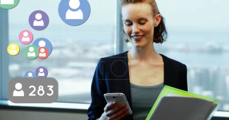 Image of digital interface with social media icons over woman using smartphone in modern office. Global digital social media network digitally generated image.