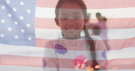 Foto de Chica Biracial sonríe detrás de una bandera americana translúcida. La superposición de la bandera simboliza la diversidad cultural y el orgullo nacional en los Estados Unidos. - Imagen libre de derechos
