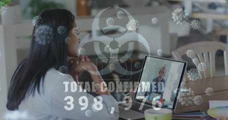 Photo for Young biracial woman looks at a laptop screen with virus graphics. The overlay suggests a discussion about a pandemic or health crisis. - Royalty Free Image