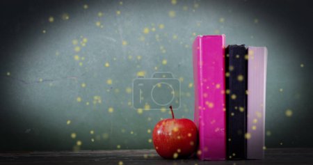 Foto de Imagen de manchas brillantes sobre manzana y libros sobre fondo verde. Día internacional de la alfabetización y concepto de lectura imagen generada digitalmente. - Imagen libre de derechos