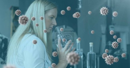 Téléchargez les photos : Image de cellules de coronavirus circulant au-dessus d'une travailleuse de laboratoire examinant des échantillons. Covid 19 pandémie santé santé science médecine concept numérique composite. - en image libre de droit