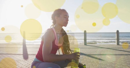 Téléchargez les photos : Image de taches jaunes sur une femme biraciale buvant de l'eau sur la promenade. concept de santé et de fitness image générée numériquement. - en image libre de droit