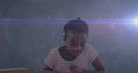 Téléchargez les photos : Image d'une écolière biraciale lisant un livre pendant un cours à l'école avec des équations flottant autour d'elle. Éducation retour à l'école et scolarisation concept digital composite. - en image libre de droit