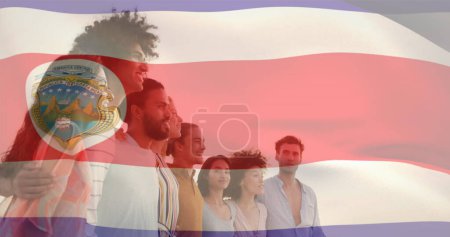Foto de Imagen de la bandera de Costa Rica ondeando sobre diversos amigos formando una cadena humana mirando al mar. Compuesto digital, exposición múltiple, unión, amistad, libertad, gobierno y patriotismo. - Imagen libre de derechos