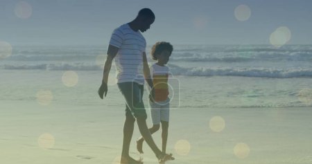 Image of light spots over african american man and his son walking together. walk day and celebration concept digitally generated image.