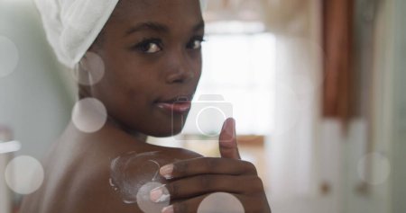 Image of african american woman using cream on body over light spots. health and beauty concept digitally generated image.