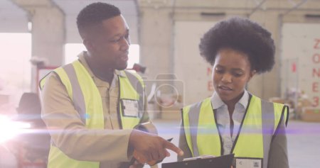 Image of glowing light over african american man and woman working in warehouse. labor day, work, workers, tradition and celebration concept digitally generated image.
